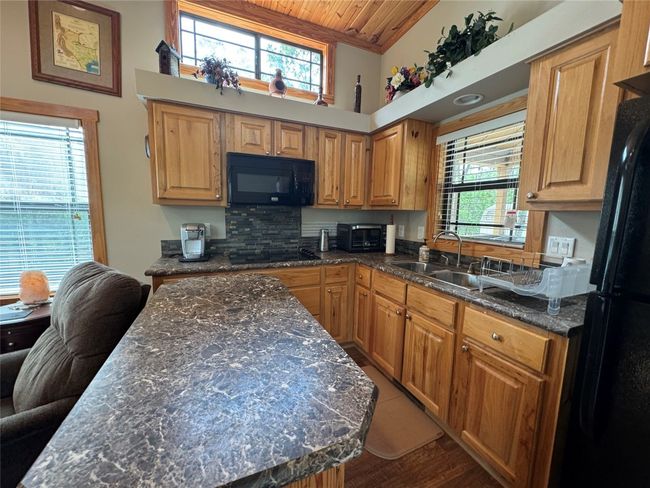 Kitchen featuring wood ceiling, black appliances, wood finished floors, dark stone countertops, and a center island | Image 28