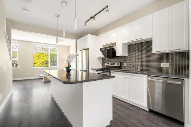 Kitchen with tasteful backsplash, appliances with stainless steel finishes, dark countertops, dark wood-style flooring, and a sink | Image 6