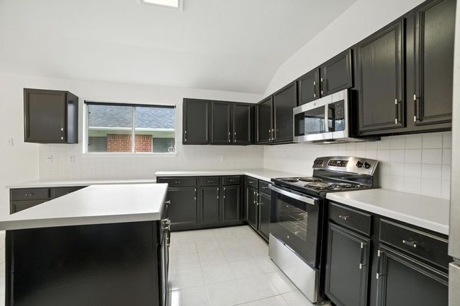 The remodeled kitchen is a true centerpiece, showcasing freshly painted cabinetry with designer hardware, abundant counter and cabinet space, a center island, built-in workstation, and brand-new stainless steel oven/range and microwave. | Image 4