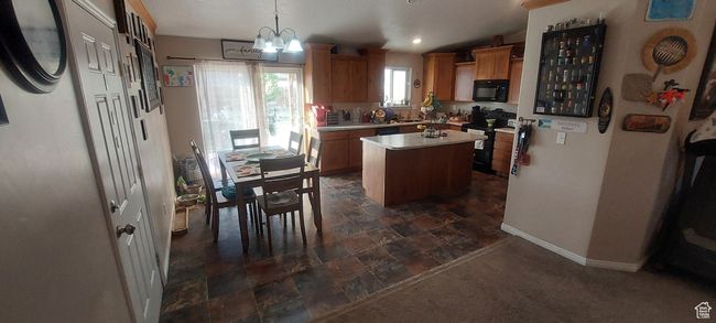 Kitchen with black appliances, a kitchen island, light countertops, a chandelier, and decorative light fixtures | Image 9