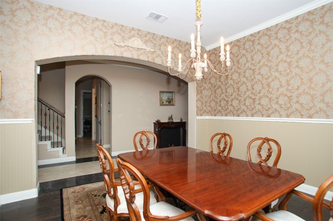 Dining space featuring wainscoting, a chandelier, arched walkways, wallpapered walls, and stairs | Image 15