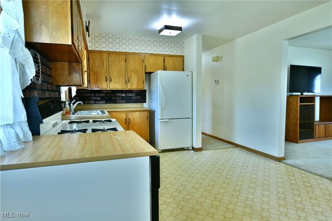 Kitchen with light carpet, a sink, freestanding refrigerator, brown cabinetry, and wood counters | Image 20