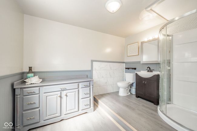 full bath with a shower stall, vanity, a wainscoted wall, toilet, and wood finished floors | Image 4
