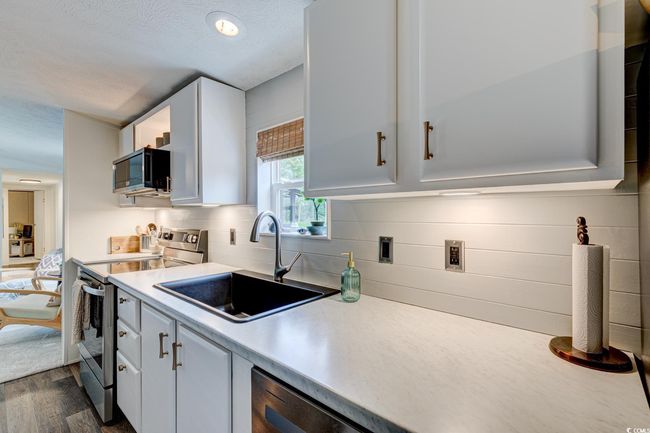 Kitchen with stainless steel range with electric stovetop, black microwave, a sink, light countertops, and dark wood-style floors | Image 12