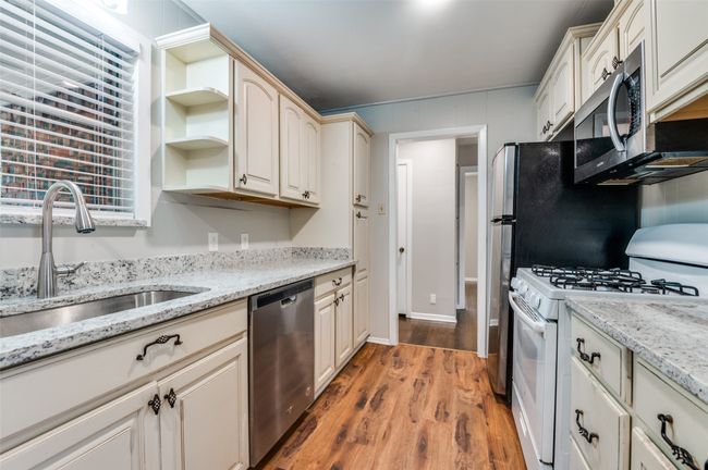 Kitchen with appliances, shelves, light wood-look flooring, and light stone counters | Image 13