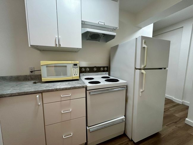 Kitchen featuring dark wood finished floors, under cabinet range hood, white cabinetry, and white appliances | Image 4