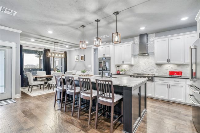 Kitchen with wall chimney exhaust hood, sink, decorative light fixtures, an island with sink, and white cabinets | Image 14