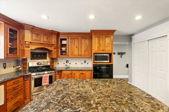 Kitchen featuring stainless steel appliances, tasteful backsplash, brown cabinets, glass insert cabinets, and recessed lighting | Image 25