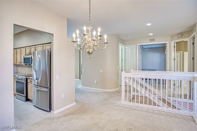 Kitchen with hanging light fixtures, stainless steel appliances, backsplash, a chandelier, and light carpet | Image 14
