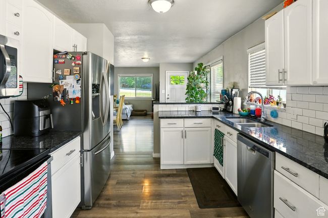 Kitchen with appliances with stainless steel finishes, dark wood-type flooring, tasteful backsplash, white cabinetry, and a peninsula | Image 9