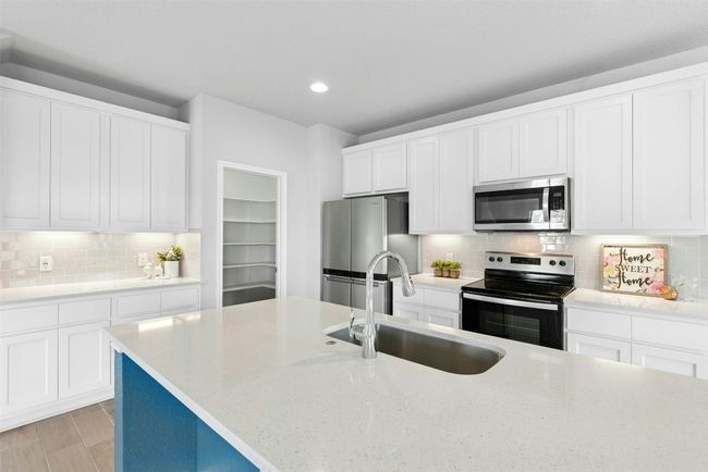 Kitchen featuring appliances with stainless steel finishes, tasteful backsplash, light stone counters, recessed lighting, and white cabinetry | Image 12