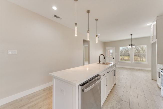 Kitchen with dishwasher, light wood-type flooring, white cabinetry, a center island with sink, and decorative light fixtures | Image 12