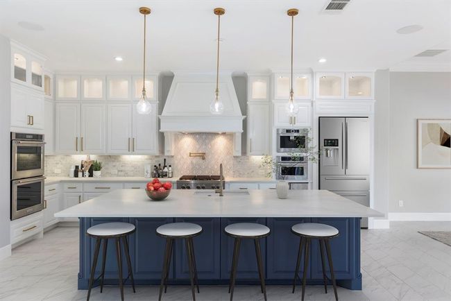 Crisp and inviting, this elegant kitchen features soft honed quartz countertops that anchor the space with a matte sophistication, beautifully complemented by a navy island, white cabinetry, and designer lighting. *This photo has been virtually staged.* | Image 9