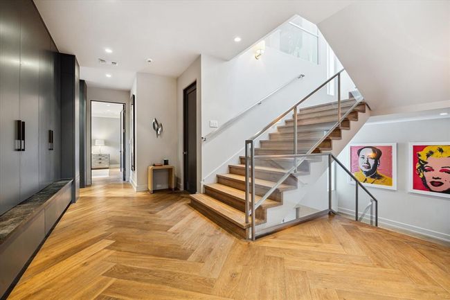 From this central landing, take the extra wide stairs, unique to this home, down to the first floor and garage, or head up to the secondary bedrooms and additional living areas. Sleek glass railings, contemporary finishes, and the elegant wide-plank herringbone flooring elevate the modern aesthetic of this hallway to a space of it's own. | Image 24