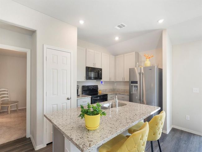 Bright and modern kitchen featuring sleek white cabinets, stainless steel appliances, and a spacious granite island with stylish yellow chairs. Perfect for cooking and entertaining. | Image 9