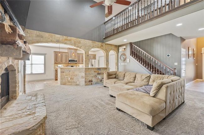 Living room with a towering ceiling, ceiling fan, arched walkways, stairway, and a stone fireplace | Image 5