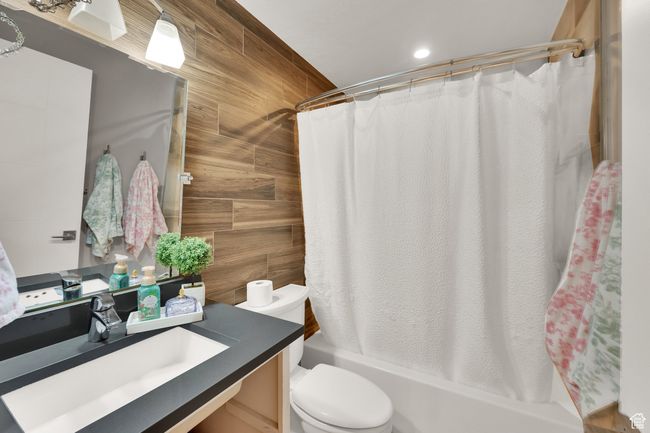 Full bath with vanity, shower / bath combo with shower curtain, wooden walls, toilet, and recessed lighting | Image 26