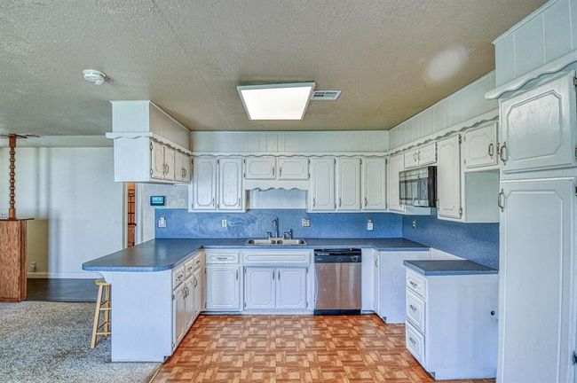 Kitchen with appliances with stainless steel finishes, a peninsula, a sink, a textured ceiling, and dark countertops | Image 7
