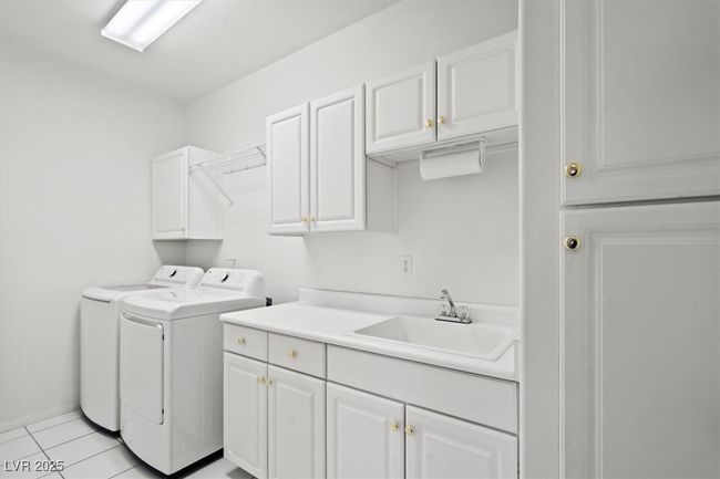 Clothes washing area featuring light tile patterned floors, baseboards, cabinet space, a sink, and washer and clothes dryer | Image 17