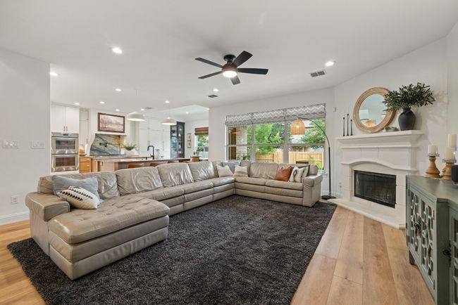 Living area with ceiling fan, light wood finished floors, a glass covered fireplace, recessed lighting, and visible vents | Image 5