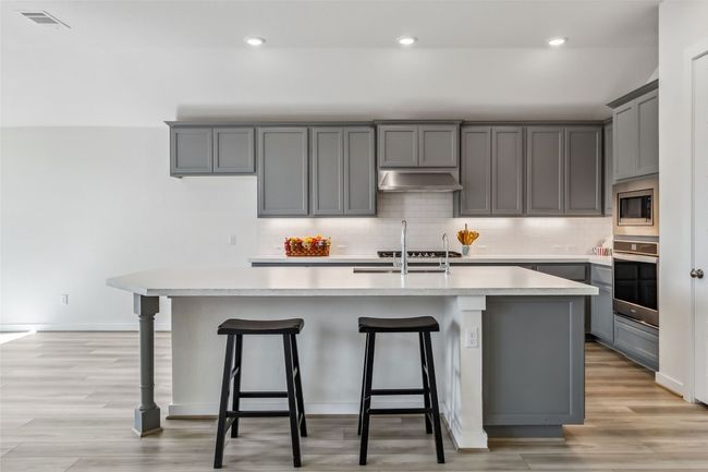 Kitchen with appliances with stainless steel finishes, under cabinet range hood, gray cabinets, light countertops, and recessed lighting | Image 11