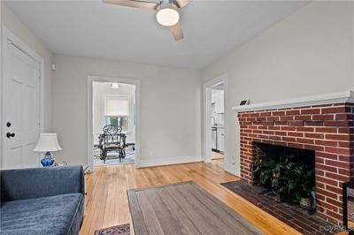 Living room with a brick fireplace, wood-type flooring, and ceiling fan | Image 2