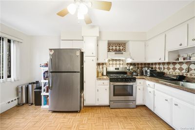 Kitchen featuring appliances with stainless steel finishes, sink, light parquet flooring, ceiling fan, and white cabinets | Image 1