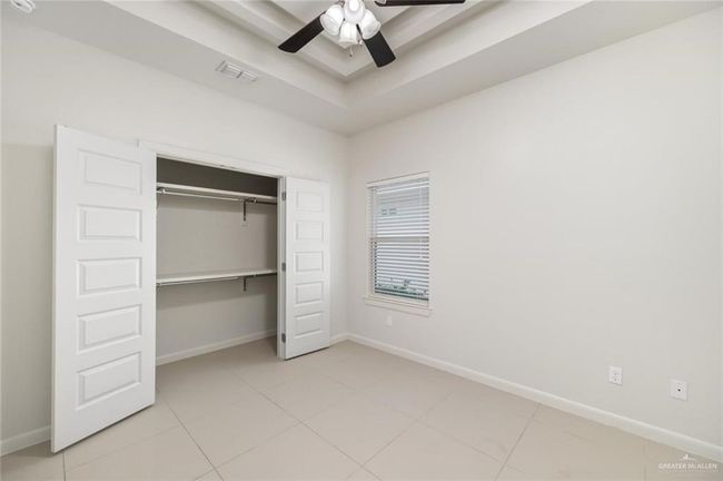 Unfurnished bedroom featuring a closet, light tile patterned flooring, ceiling fan, and a tray ceiling | Image 5