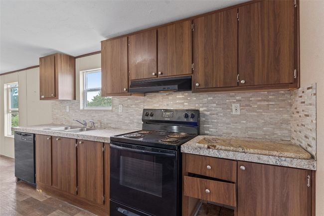 Kitchen featuring under cabinet range hood, black appliances, light countertops, tasteful backsplash, and wood finished floors | Image 16