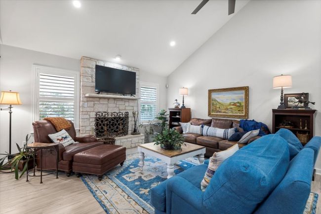 Living room with ceiling fan, wood finished floors, high vaulted ceiling, a stone fireplace, and recessed lighting | Image 12