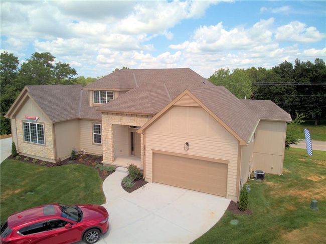 View of front of home with stone siding, roof with shingles, a front yard, concrete driveway, and a porch | Image 5
