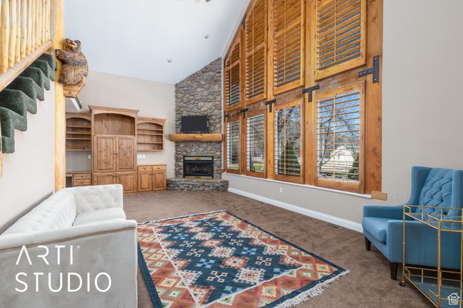 Carpeted living room featuring a stone fireplace, a high ceiling, and baseboards | Image 17