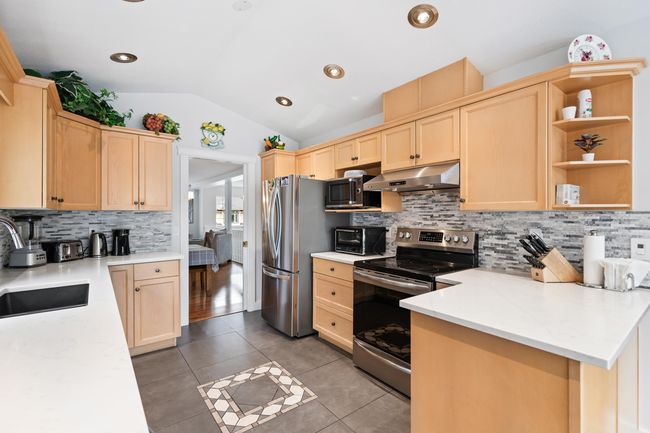 Kitchen featuring appliances with stainless steel finishes, under cabinet range hood, light brown cabinetry, vaulted ceiling, and decorative backsplash | Image 9