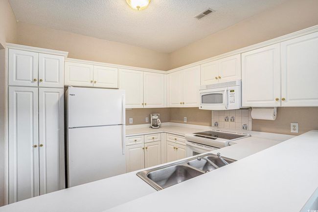 Kitchen featuring white appliances, a sink, white cabinets, and a textured ceiling | Image 6
