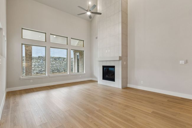 Unfurnished living room featuring light wood-type flooring, ceiling fan, a tile fireplace, and a towering ceiling | Image 12