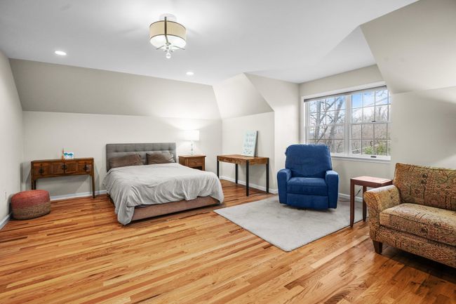 This spacious en suite bedroom features charming architectural angles, rich hardwood flooring, and plenty of space for a seating or reading area near the large window that fills the room with natural light. | Image 31