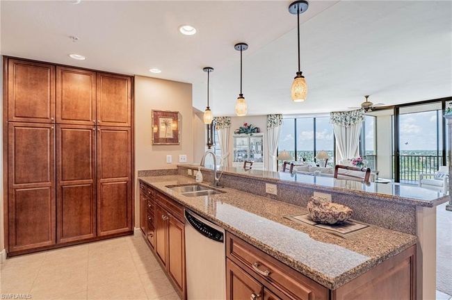 Kitchen featuring light tile patterned flooring, dishwasher, light stone counters, decorative light fixtures, and sink | Image 20