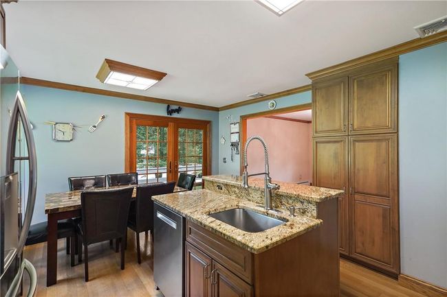 Kitchen featuring stainless steel appliances, sink, light hardwood / wood-style floors, light stone countertops, and an island with sink | Image 11