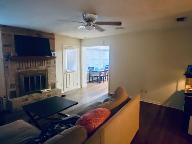 Living room featuring ceiling fan, wood finished floors, visible vents, baseboards, and a brick fireplace | Image 7