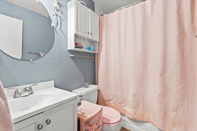 Bathroom featuring a textured wall, toilet, vanity, and shower / bathtub combination with curtain | Image 11