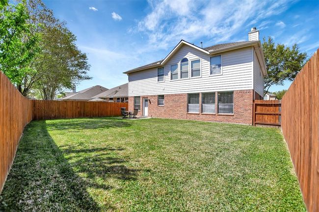 This photo showcases a spacious backyard with well-maintained grass, enclosed by a wooden fence for privacy. The back of a two-story house is visible, featuring a combination of brick and siding with large windows. | Image 44