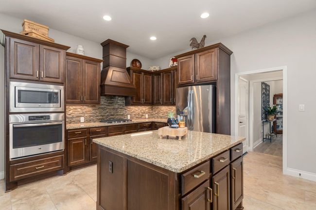This stunning kitchen displays such a beautiful contrast with the dark stained cabinets, neutral paint, granite countertops, tile backsplash, SS appliances, kitchen island with extra storage, breakfast bar, recessed lighting, high ceilings and walk in pantry. | Image 14