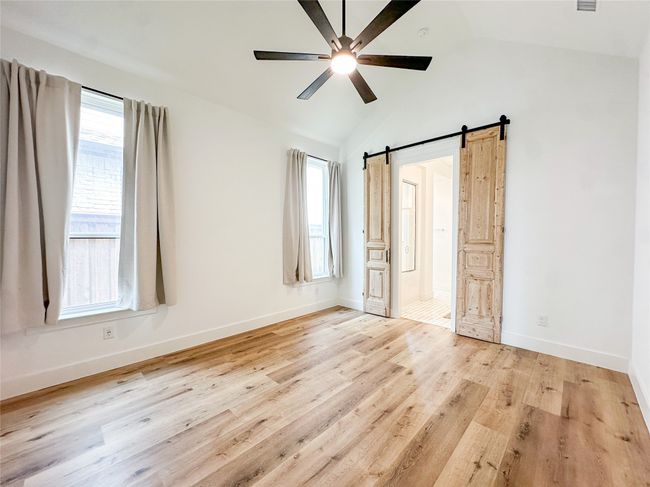 Unfurnished bedroom with a barn door, vaulted ceiling, light wood-style flooring, connected bathroom, and a ceiling fan | Image 18