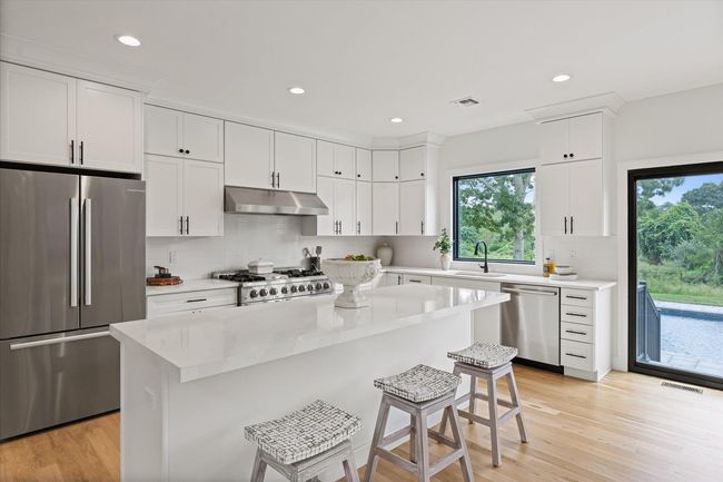 Kitchen featuring sink, appliances with stainless steel finishes, a center island, white cabinets, and a kitchen bar | Image 14