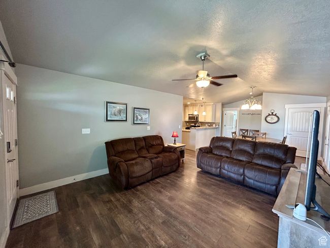 Living area with lofted ceiling, dark wood-type flooring, a chandelier, ceiling fan, and baseboards | Image 8
