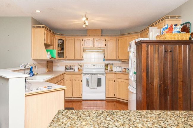Kitchen featuring white range with electric cooktop, backsplash, light countertops, under cabinet range hood, and a sink | Image 8