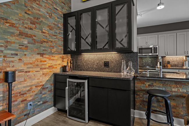 Indoor bar with beverage cooler, stainless steel microwave, backsplash, and wood finished floors | Image 10