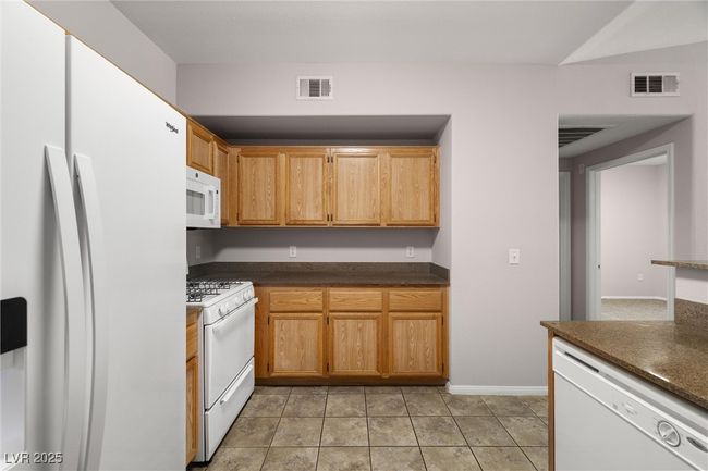 Kitchen with baseboards, visible vents, white appliances, and dark countertops | Image 20