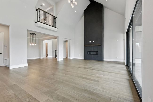 Unfurnished living room with high vaulted ceiling, light wood-style floors, a fireplace, and a chandelier | Image 10