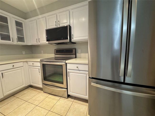 Kitchen with appliances with stainless steel finishes, white cabinetry, light countertops, light tile patterned floors, and glass insert cabinets | Image 7